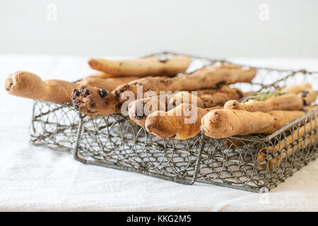 Frisch gebackenes Brot, hausgemachte grissini Sticks in vintage Metallgitter auf weißen Tischdecke. Tageslicht. Stockfoto