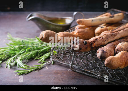 Frisch gebackenes Brot, hausgemachte grissini Sticks in Vintage metal grid Box mit Olivenöl und Kräuter Rosmarin und Thymian über dunkle Oberfläche. Stockfoto