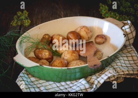 Gebratene junge Kartoffeln mit Holzspachtel und frischem Dill in Metall pan. Über schwarzen Holztisch mit karierten Küchenhandtuch. dunklen rustikalen Stil. Stockfoto