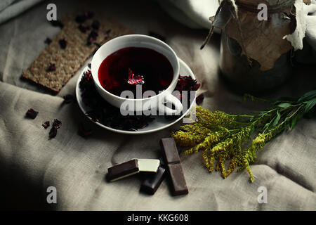 Blick von oben auf weißem Porzellan Glas Tasse roter Tee karkade auf Leinwand Tischdecke. hausgemachten Schokoladenkekse, Zitrone, Zimt, Honig und thuj Stockfoto