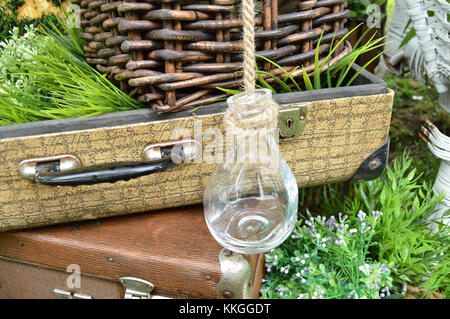 Schönes Design im Park - vintage Koffer mit Flaschen, Platten und Warenkorb auf Gras. Stockfoto