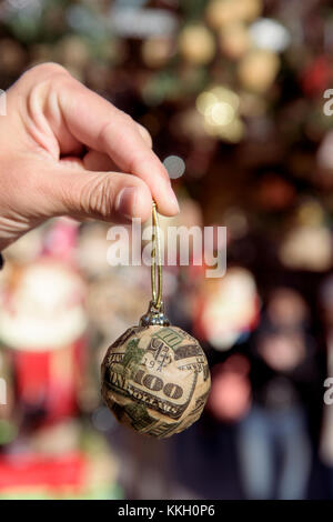 Nahaufnahme von einem jungen Mann mit einem christmas Ball auf Stücke von uns 100 Dollar Bill in einem Weihnachtsmarkt gewickelt Stockfoto