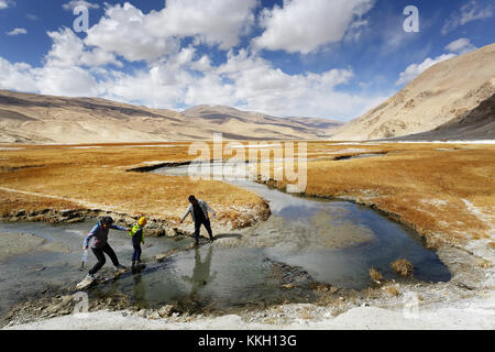 Drei Menschen einander helfen, überqueren einen Stream bei den heißen Quellen, Geysir, der Puga, Ladakh, Jammu und Kaschmir, Indien. Stockfoto