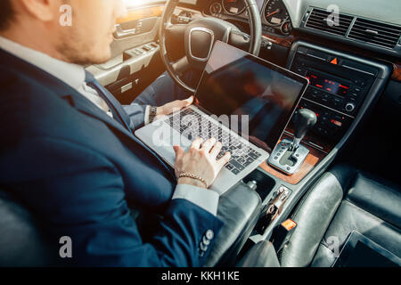 Ernsthafte Geschäftsmann in einem Auto mit Laptop Stockfoto