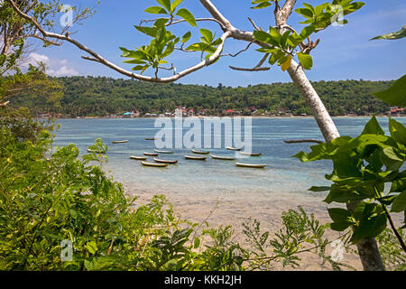 Fischerboote und Blick über Dorf an der Küste auf der Insel Nusa Ceningan von Nusa Lembongan in der Nähe von Bali in Indonesien gesehen Stockfoto