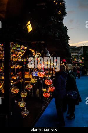 Edinburgh, Schottland, Vereinigtes Königreich, 30. November 2017. Edinburgh Weihnachtsfeier Weihnachtsmarkt. Eine Gruppe von Frauen Durchsuchen der Weihnachtsmarkt Stände und eine Laterne. Zentrum der Stadt ist beleuchtet mit wunderschönen farbigen Lichtern bei Sonnenuntergang an einem Winterabend Stockfoto