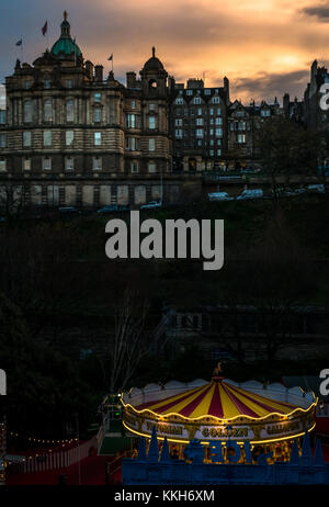 Edinburgh, Schottland, Vereinigtes Königreich, 30. November 2017. Edinburgh Weihnachtsfeiern gehören ein Weihnachtsmarkt und Fahrgeschäfte. Zentrum der Stadt ist beleuchtet mit bunten Lichtern von einem Karussell in der Princes Street Gardens als es dunkel an einem Winterabend erhält, mit Blick auf die imposanten Wahrzeichen viktorianischen Gebäude Bank von Schottland (Lloyds Banking Group) Sitz auf dem Damm bis in der Dämmerung leuchtet Stockfoto
