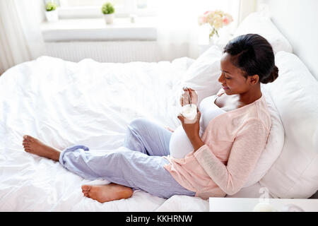 Schwangere Frau isst Joghurt im Bett Stockfoto