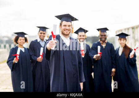 glückliche Schüler in Mörtel-Boards mit Diplomen Stockfoto