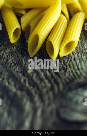 In der Nähe von hellen gelben Nudeln Penne auf einer hölzernen Hintergrund Stockfoto