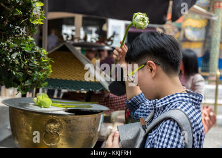 Bangkok, Thailand. Anbeter Besprengung heiliges Wasser auf dem Kopf mit einer Lotusblüte, Royal Grand Palace Compound. Stockfoto