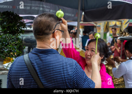 Bangkok, Thailand. Anbeter Besprengung heiliges Wasser auf dem Kopf mit einer Lotusblüte, Royal Grand Palace Compound. Stockfoto