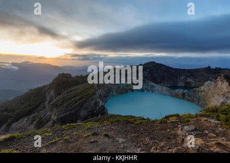 Nebel beginnt zu bilden, wie die Sonne über zwei kraterseen am Kelimutu Nationalpark in Ost Nusa Tenggara, Indonesien steigt. Stockfoto