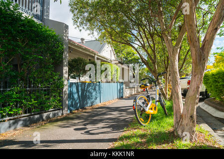 Sydney, Australien - 23 November, 2017; Stadt mit Bäumen gesäumten Vorstadtstraße mit gelben Fahrrad teilen Zyklus stehen gelassen. Stockfoto