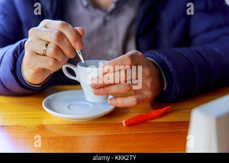 Mann mit Tasse Kaffee. Junge männliche Person in Freizeitkleidung in heißes Getränk im Cafe und Fenster auf sonnigen Tag Stockfoto