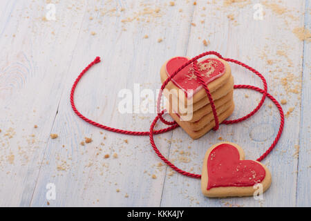 Rote herzförmige Plätzchen in der angeschlossenen Band auf Holzbrettern close-up auf Valentinstag Stockfoto