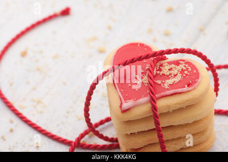 Rote herzförmige Plätzchen in der angeschlossenen Band auf Holzbrettern close-up auf Valentinstag Stockfoto