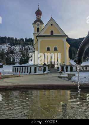 Kleine Kirche in Going am Wilden Kaiser auf einer winterlichen Nachmittag mit Wassertropfen von einem Brunnen Stockfoto