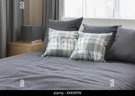 Schlafzimmer-Innenarchitektur mit aufgegebenen grüne Kissen auf graue Bett und dekorative Tischleuchte. Stockfoto