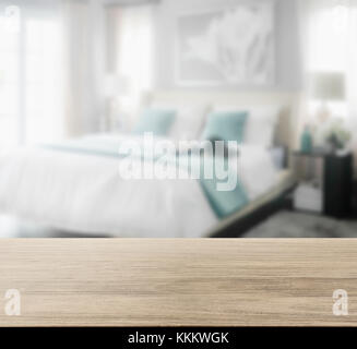 Holz- Tischplatte mit Unschärfe des gemütlichen Schlafzimmer Einrichtung mit weißen und grünen Kissen auf dem Bett Stockfoto