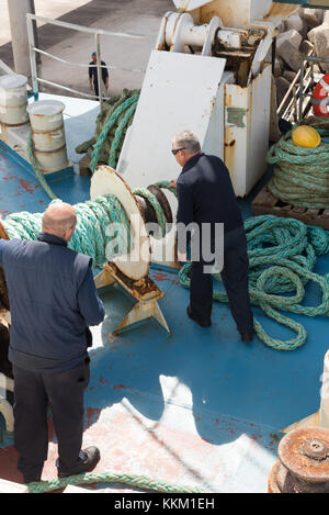 Arbeiter auf Gozo Channel Line Fähre Maschinen bedienen und wickeln Seil um eine Winde, als das Schiff den Hafen verlässt. Stockfoto