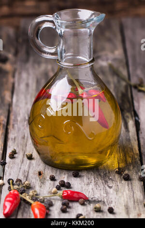 Glas Flasche Olivenöl mit red hot chili peppers über alte hölzerne Hintergrund. siehe Serie Stockfoto