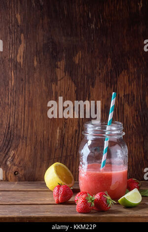 Glas Glas mit Rote Erdbeere Smoothie, serviert mit frischen Erdbeeren, Zitrone und Limette über Holz- Tabelle Stockfoto