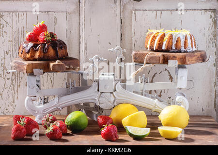 Hausgemachte Schokolade Kuchen mit Erdbeeren und dunkle Schokolade ganache, und weißem Zuckerguss und Zitronenschale, auf vintage Waagen über Holz- Tabelle w serviert. Stockfoto