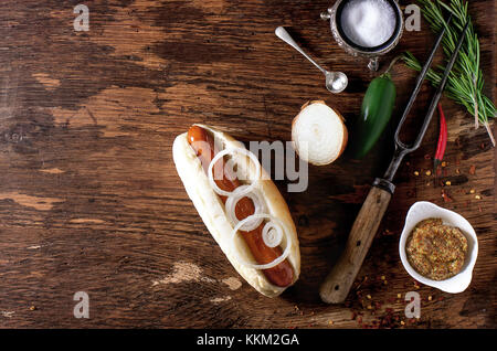 Hausgemachte Hot Dog mit Zutaten Senf, Tomatenmark, Zwiebeln, Chili, Rosmarin. Auf Holztisch mit Fleisch Gabel und Löffel. Rahmen mit Kopie spac Stockfoto