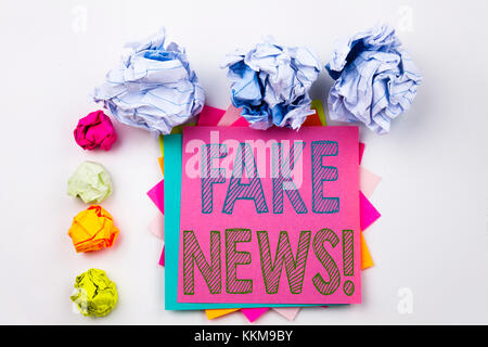 Schreiben eines Textes mit Fake News, geschrieben auf Haftnotiz im Büro mit Schraubenpapierkugeln. Geschäftskonzept für Propagandazeitung Fake News auf weißem i Stockfoto
