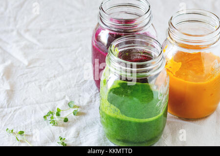 Sortiment an Gemüse Smoothies aus Karotte, rote Beete und Spinat, die in Gläsern. über weiße Tischdecke. rustikalen Stil, Tageslicht Stockfoto