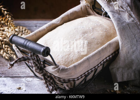 Brot backen. Teig in proofing Warenkorb auf Holztisch mit Mehl und Weizen Ohren. Stockfoto