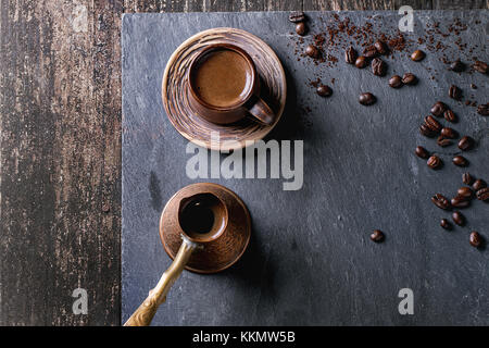 Braun Keramik Tasse Kaffee, alte Kupfer cezve und Kaffeebohnen. Über schwarzem Schiefer als Hintergrund. mit Kopie Raum im Zentrum. Ansicht von oben. Stockfoto