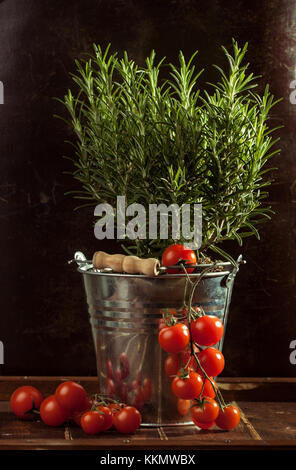 Cherry Tomaten mit Haufen Rosmarin in Metall Eimer auf hölzernen Tisch Stockfoto