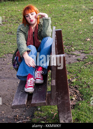 Rothaarige Mädchen auf der Bank im Park im Herbst Stockfoto