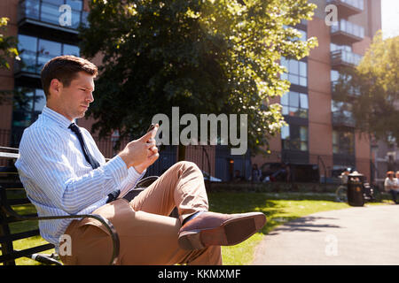 Unternehmer im Freien mit Handy auf Mittagspause im Park Stockfoto