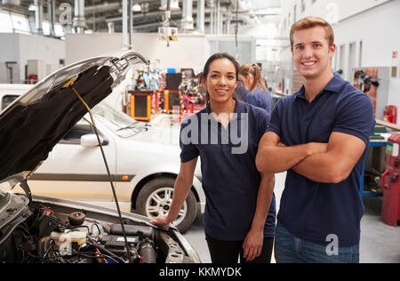 Zwei Auszubildende der Mechanik zur Kamera schaut neben einem Auto Stockfoto