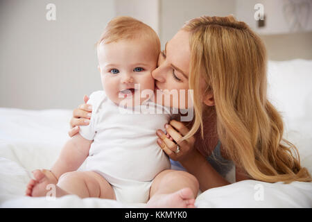 Mutter lag auf dem Bett zu Hause gibt Baby Sohn Kuss Stockfoto