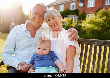 Großeltern auf Sitz im Garten mit Baby Enkel Stockfoto