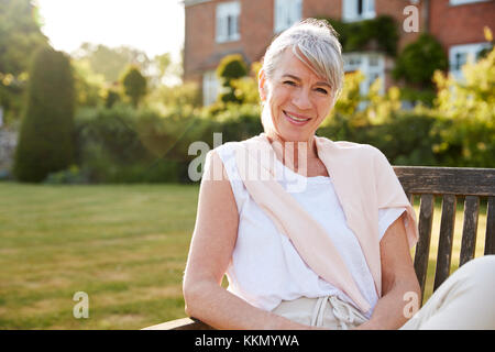Ältere Frau sitzt auf der Gartenbank in der Abendsonne Stockfoto