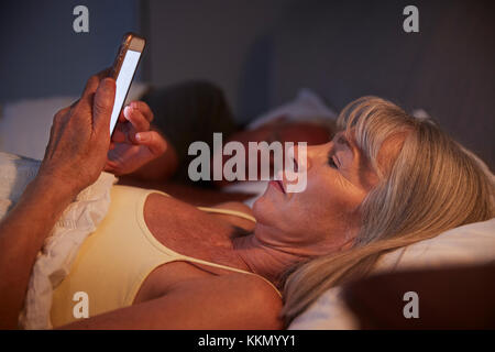 Schlaflose ältere Frau im Bett in der Nacht über Mobiltelefon Stockfoto