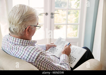 Älterer Mann sitzt in einem Sessel Kreuzworträtsel zu tun, in der Nähe Stockfoto