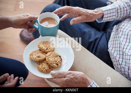 Frau übergibt Tee und Gebäck zu Sitzender älterer Mann, Detail Stockfoto