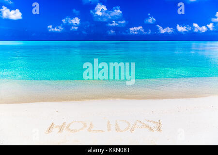 Wort Urlaub auf Sand in Malediven geschrieben mit der Lagune im Hintergrund. Stockfoto