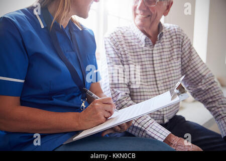 Älterer Mann sitzt mit Krankenschwester Noten Seniorenheim, Stockfoto