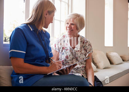 Ältere Frau sitzt mit Krankenschwester Noten Seniorenheim, Stockfoto