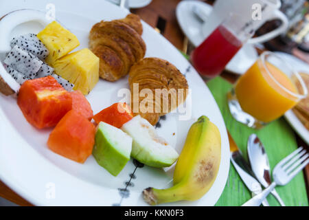 Leckeren, gesunden Frühstück im Freien an einem hölzernen Tisch mit Blick auf das Meer im Hintergrund. Das Frühstück besteht aus frischem Obst und Waffeln mit Pfannkuchen. Stockfoto