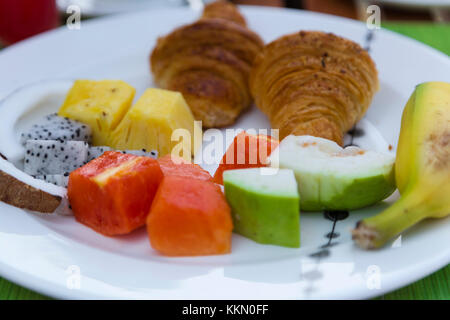 Leckeren, gesunden Frühstück im Freien an einem hölzernen Tisch mit Blick auf das Meer im Hintergrund. Das Frühstück besteht aus frischem Obst und Waffeln mit Pfannkuchen. Stockfoto