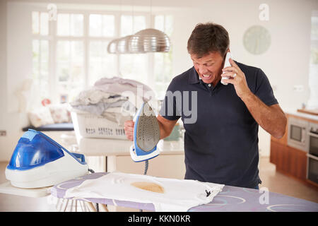 Im mittleren Alter Mann per Telefon abgelenkt beim Bügeln Hemd brennt Stockfoto