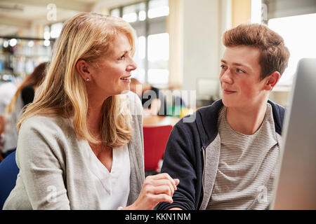 Lehrer mit männlichen Schüler Arbeiten am Computer in der Hochschule Bibliothek Stockfoto